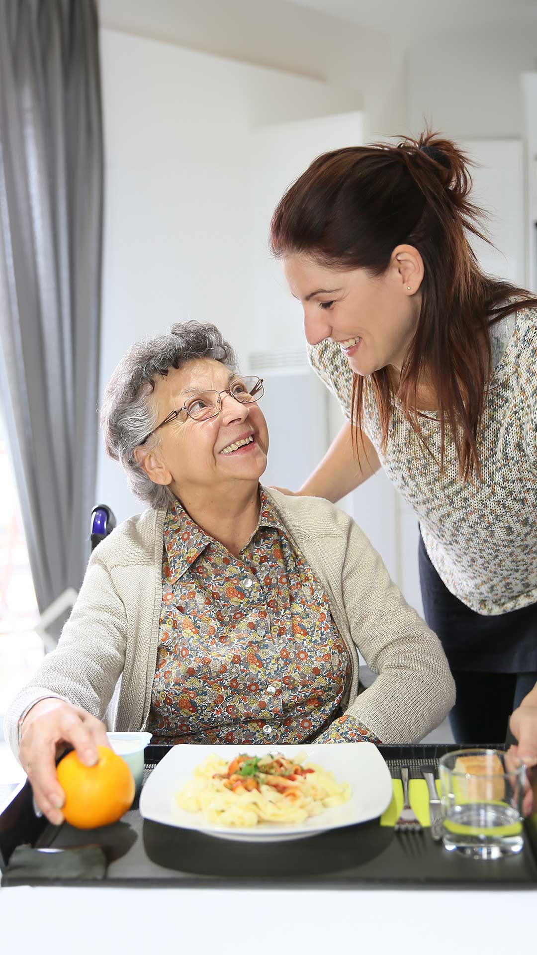 Young woman happily talking to a smiling senior in front of a meal