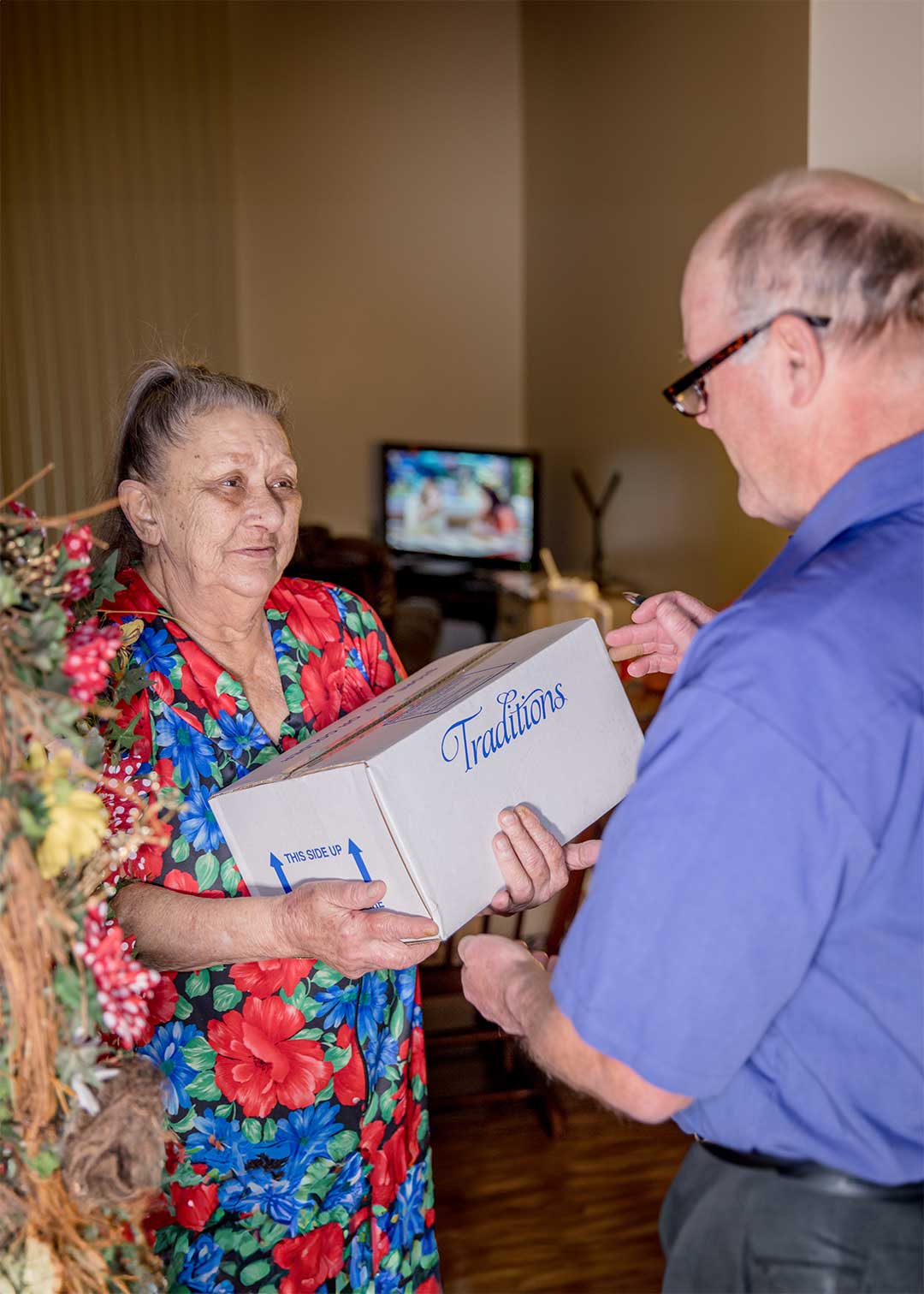 A delivery driver handing box of Traditions Frozen Meal solutions to person in home