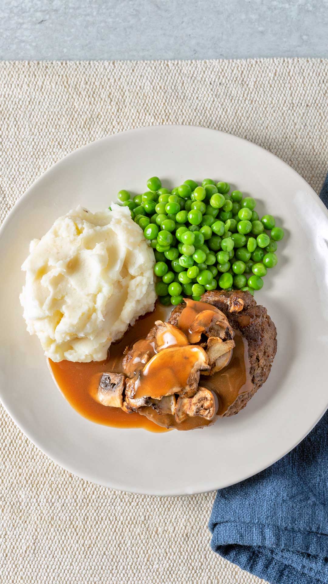 Overhead plated view of Traditons Meals pork patty with mushroom gravy, mashed potatoes and peas.